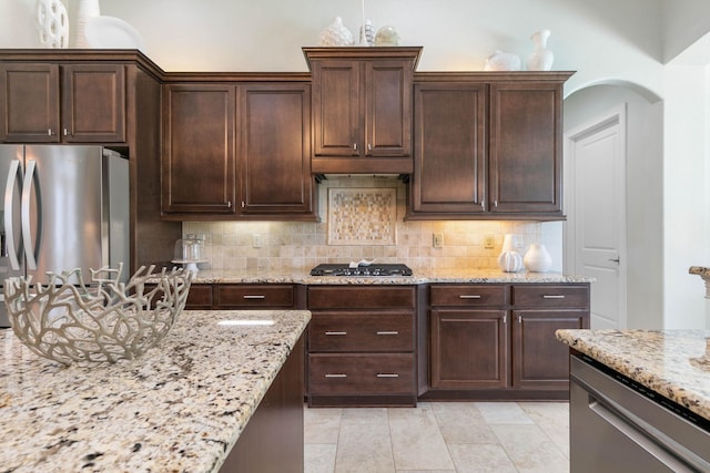 kitchen featuring tasteful backsplash, appliances with stainless steel finishes, light stone counters, and dark brown cabinetry