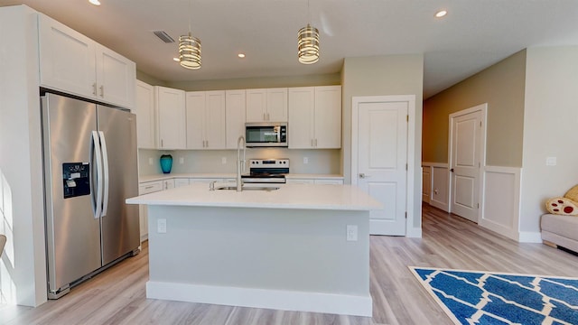 kitchen with hanging light fixtures, appliances with stainless steel finishes, a kitchen island with sink, and white cabinets