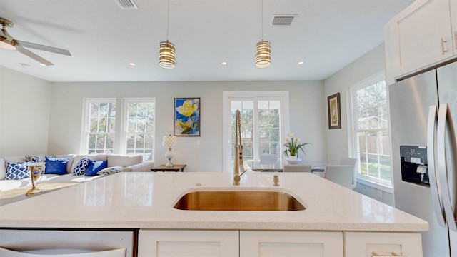 kitchen featuring stainless steel refrigerator with ice dispenser, white cabinets, light stone counters, and pendant lighting