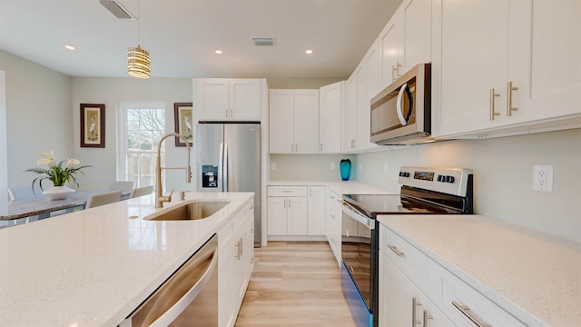 kitchen featuring decorative light fixtures, white cabinetry, stainless steel appliances, light stone countertops, and light hardwood / wood-style flooring