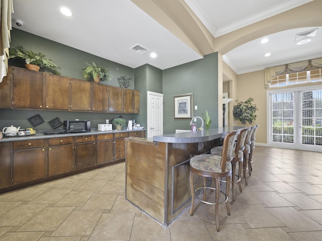 kitchen with a breakfast bar area, ornamental molding, dark brown cabinetry, a center island with sink, and french doors