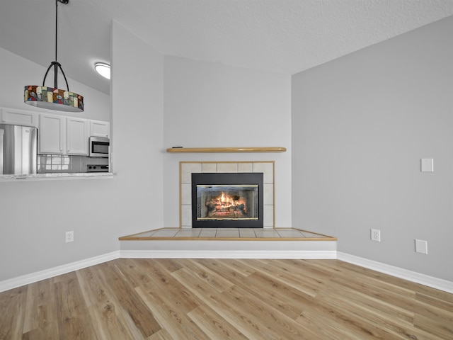 unfurnished living room featuring a textured ceiling, a tiled fireplace, baseboards, and wood finished floors