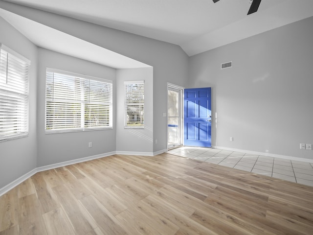 empty room featuring lofted ceiling, visible vents, light wood-style flooring, ceiling fan, and baseboards