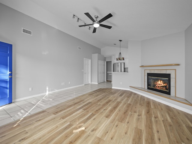 unfurnished living room with lofted ceiling, visible vents, a tiled fireplace, and tile patterned floors