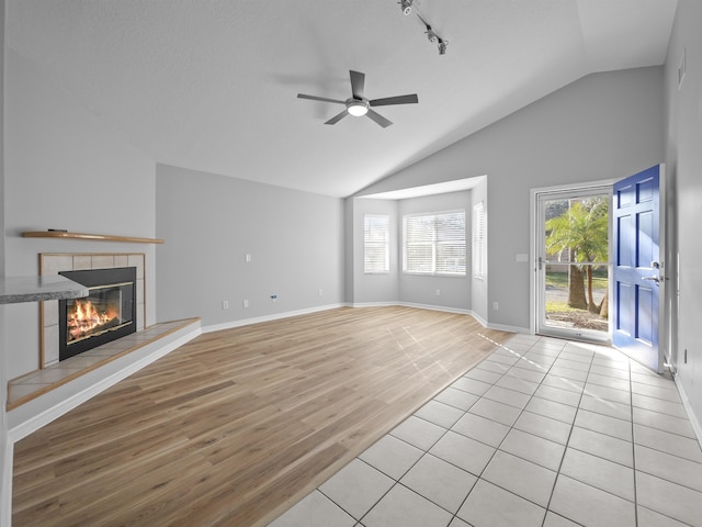 unfurnished living room featuring a fireplace, a ceiling fan, baseboards, vaulted ceiling, and light wood-style floors