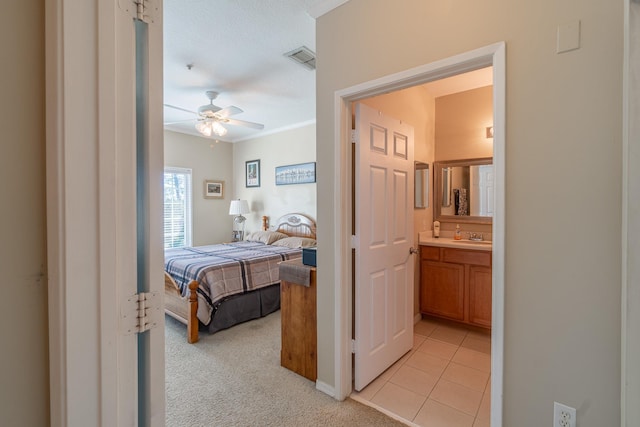 carpeted bedroom featuring sink, ensuite bathroom, ceiling fan, and ornamental molding