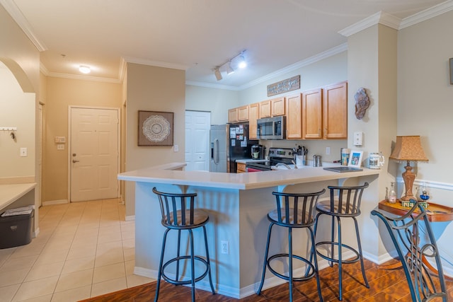 kitchen featuring rail lighting, appliances with stainless steel finishes, kitchen peninsula, light tile patterned floors, and a breakfast bar