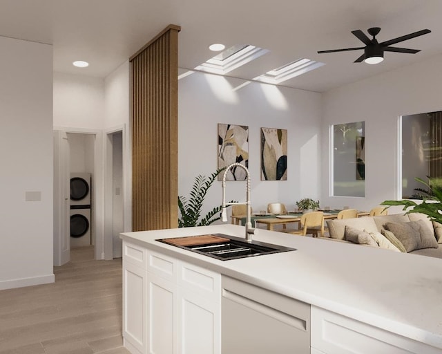 kitchen with sink, stacked washer / dryer, white dishwasher, light hardwood / wood-style floors, and white cabinets