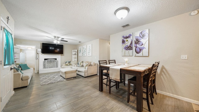 11428 Rustic Pines Cir, Jacksonville, FL 32257 - dining room with a textured ceiling, a ceiling fan, a brick fireplace, wood finished floors, and baseboards