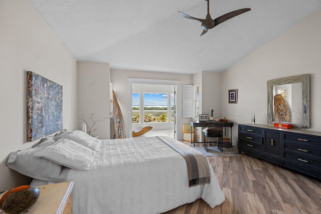 bedroom with vaulted ceiling, a textured ceiling, ceiling fan, and wood finished floors