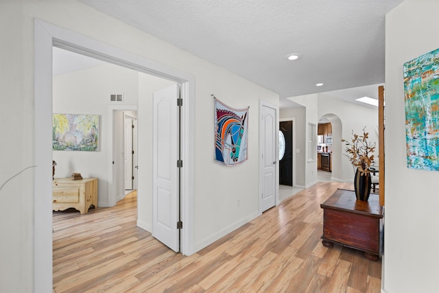 corridor with arched walkways, visible vents, a textured ceiling, and light wood-type flooring