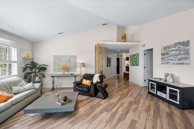 living area with vaulted ceiling, wood finished floors, visible vents, and a textured ceiling