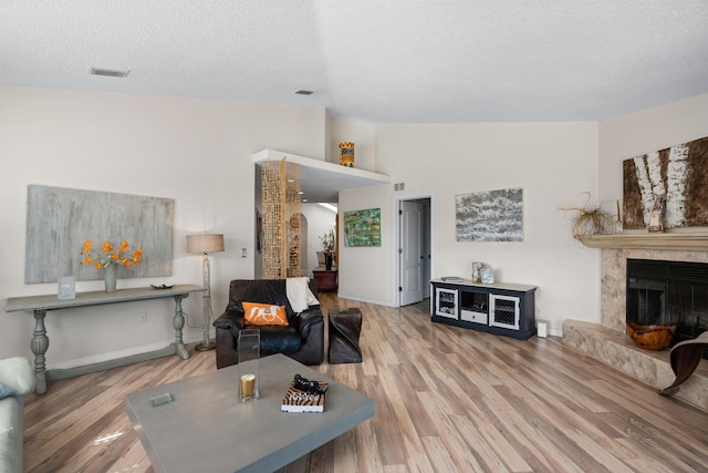 living room with vaulted ceiling, wood finished floors, a fireplace with raised hearth, and a textured ceiling