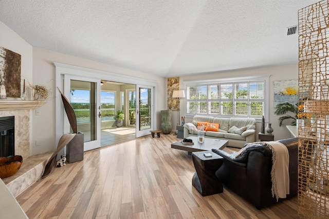 living area with a premium fireplace, a textured ceiling, visible vents, and wood finished floors