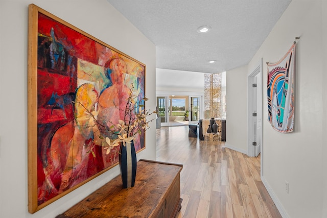 hallway featuring light wood-style flooring, recessed lighting, baseboards, and a textured ceiling