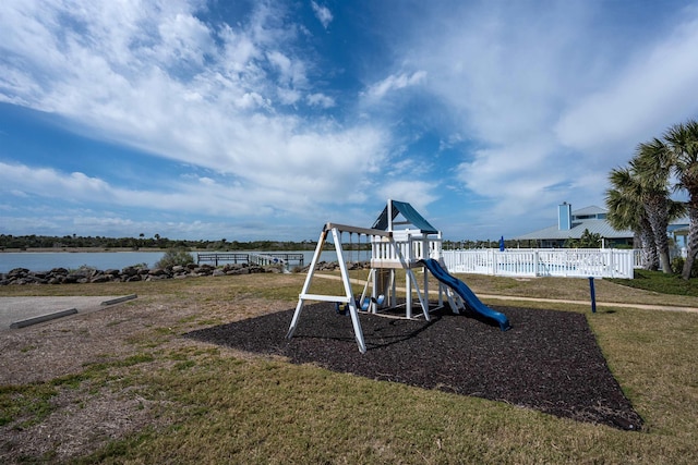 community playground with fence, a water view, and a lawn