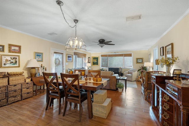 dining space with crown molding, wood-type flooring, and ceiling fan with notable chandelier