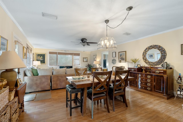 dining space featuring ceiling fan with notable chandelier, light hardwood / wood-style flooring, and crown molding