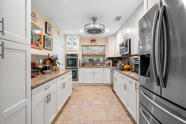 kitchen with light stone countertops, stainless steel appliances, light tile patterned floors, tasteful backsplash, and white cabinets