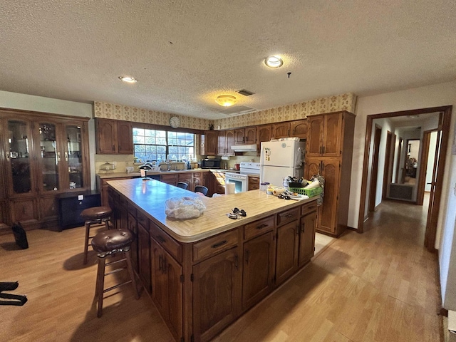 kitchen with white appliances, light hardwood / wood-style flooring, a textured ceiling, a kitchen island, and a kitchen bar