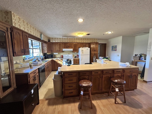 kitchen with a kitchen bar, sink, white appliances, and light wood-type flooring