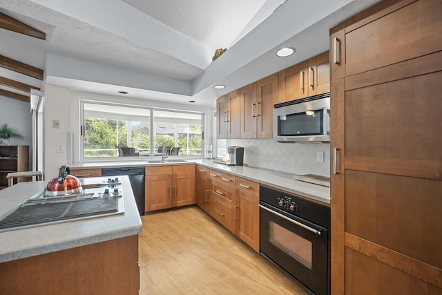 kitchen featuring tasteful backsplash, brown cabinets, light countertops, black appliances, and a sink