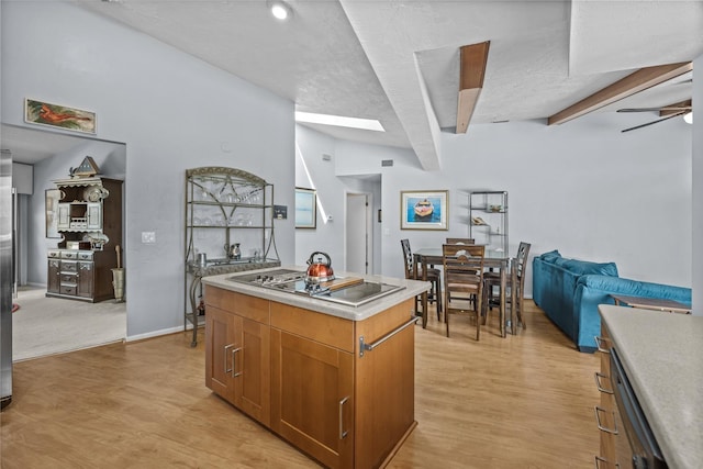 kitchen featuring brown cabinetry, a ceiling fan, a center island, black electric cooktop, and light countertops