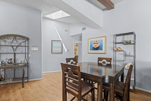 dining room with baseboards, vaulted ceiling with skylight, visible vents, and light wood-style floors