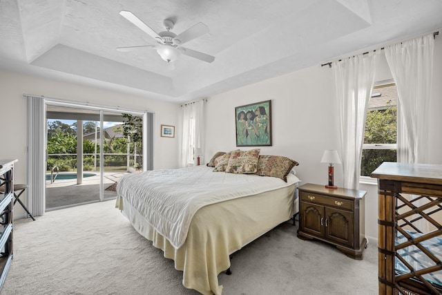 bedroom featuring access to exterior, ceiling fan, a tray ceiling, and light colored carpet