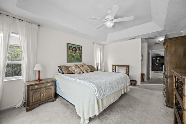 bedroom with a tray ceiling, light carpet, ceiling fan, and visible vents