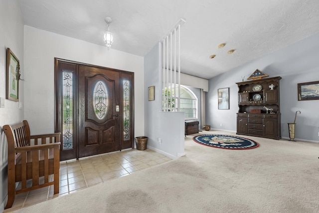 foyer entrance featuring lofted ceiling, light tile patterned floors, a textured ceiling, light colored carpet, and baseboards