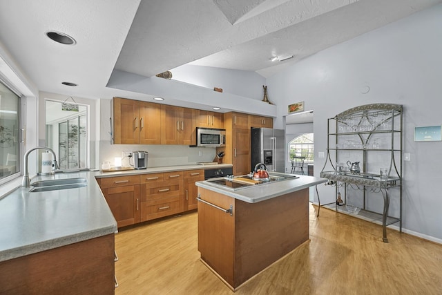 kitchen featuring a kitchen island with sink, stainless steel appliances, a sink, light countertops, and brown cabinets