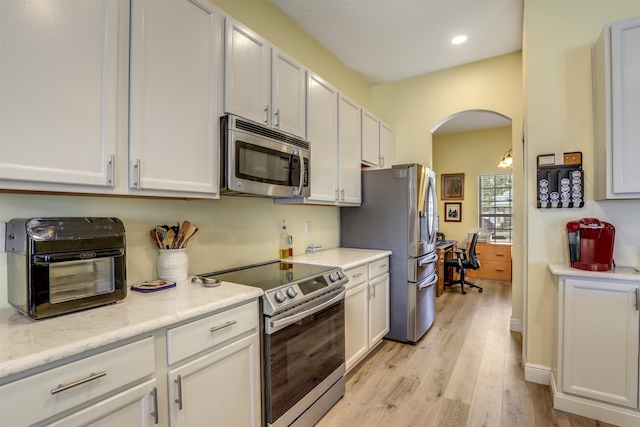 kitchen with arched walkways, recessed lighting, stainless steel appliances, white cabinetry, and light wood-style floors