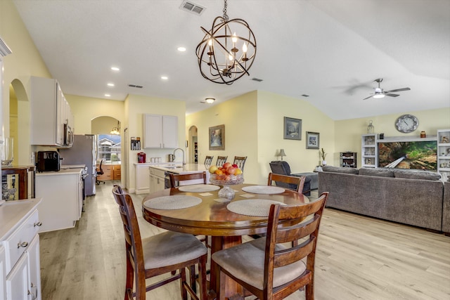 dining space with light wood-style floors, visible vents, arched walkways, and vaulted ceiling