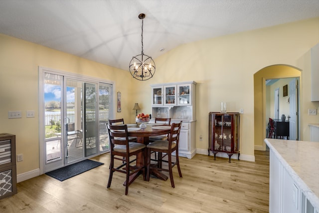 dining space with arched walkways, vaulted ceiling, light wood-style flooring, and baseboards