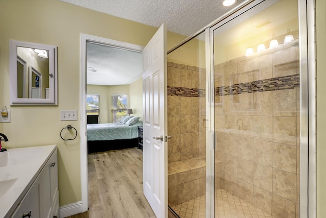 ensuite bathroom with ensuite bath, wood finished floors, a textured ceiling, vanity, and a shower stall