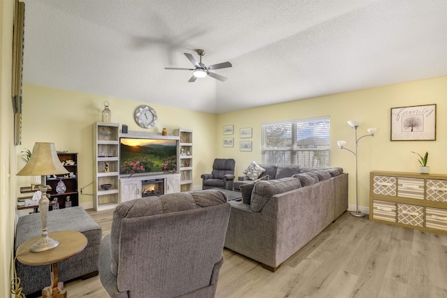 living area with a textured ceiling, ceiling fan, light wood-style flooring, baseboards, and a glass covered fireplace