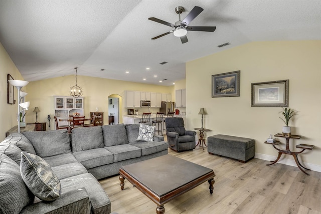 living area featuring lofted ceiling, light wood-style floors, visible vents, and arched walkways