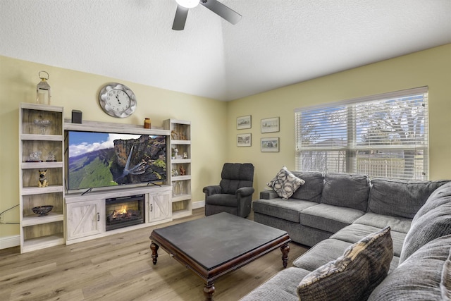 living room featuring a glass covered fireplace, ceiling fan, a textured ceiling, wood finished floors, and baseboards