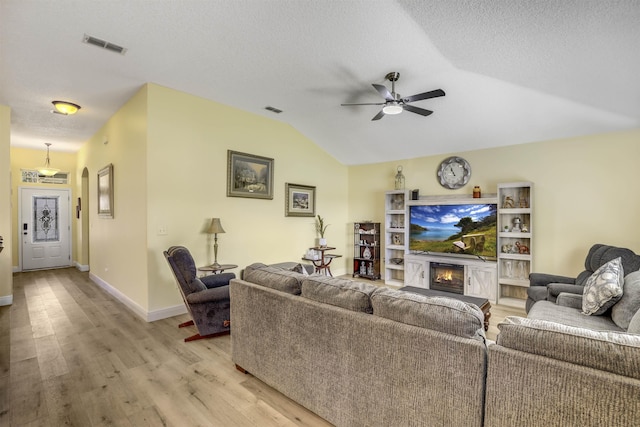 living room with light wood-style floors, lofted ceiling, visible vents, and a glass covered fireplace