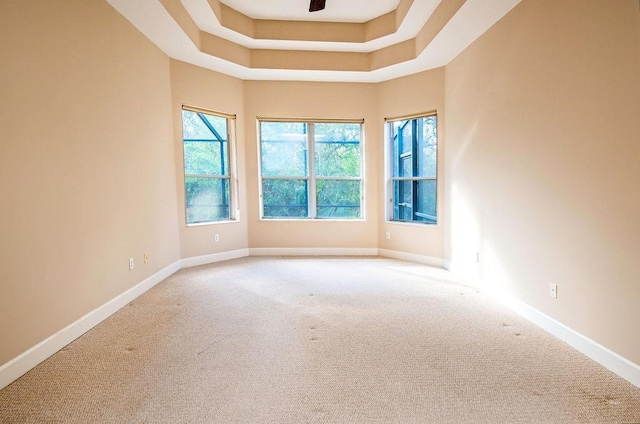 carpeted empty room with a raised ceiling, ceiling fan, and a healthy amount of sunlight