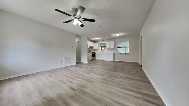 unfurnished living room featuring ceiling fan, light wood-type flooring, and a textured ceiling