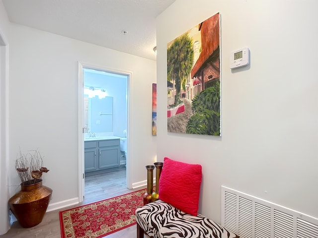 hallway featuring visible vents, a sink, baseboards, and wood finished floors