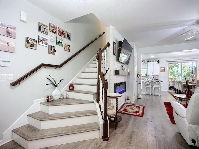 staircase with a large fireplace, wood finished floors, and baseboards