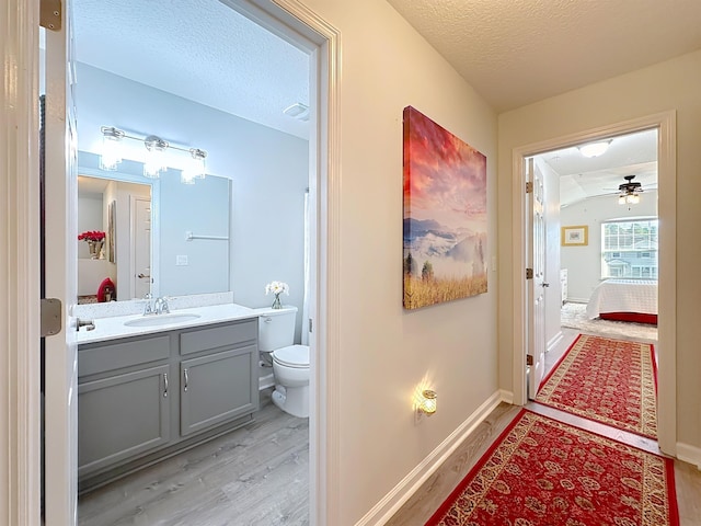 bathroom featuring baseboards, toilet, wood finished floors, a textured ceiling, and vanity