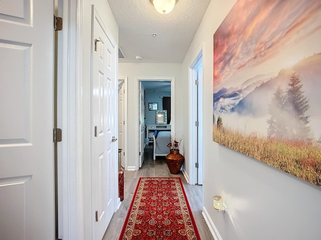 corridor with visible vents, a textured ceiling, baseboards, and wood finished floors