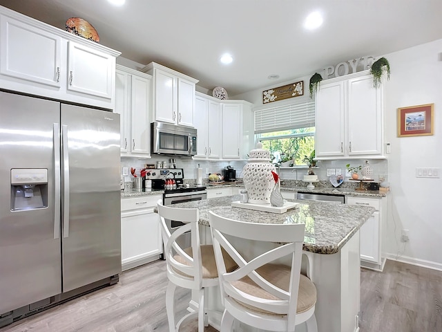 kitchen with tasteful backsplash, appliances with stainless steel finishes, white cabinets, and light wood-style flooring