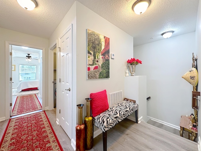 hall featuring light wood-type flooring, baseboards, visible vents, and a textured ceiling