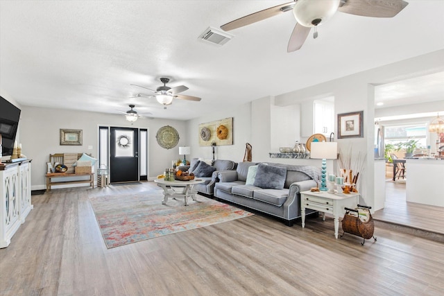 living room featuring ceiling fan, light hardwood / wood-style flooring, and a textured ceiling