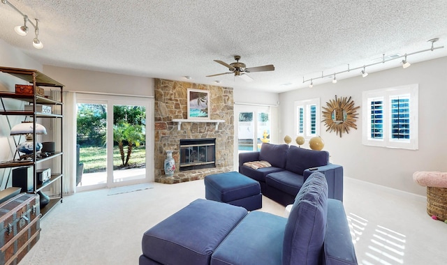 carpeted living area with rail lighting, plenty of natural light, a textured ceiling, and a stone fireplace